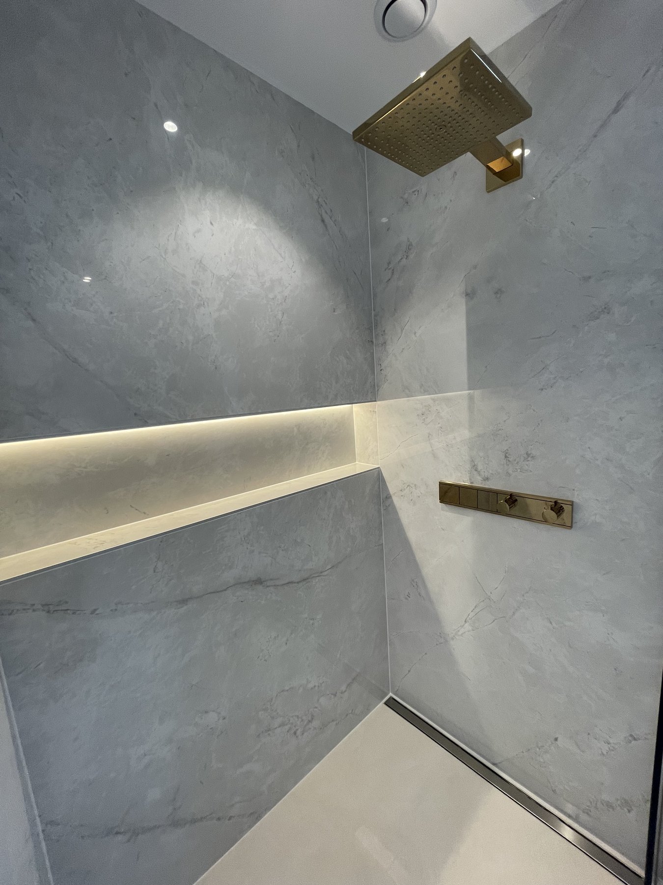 Douche à l'italienne en grand format gris, niche éclairée et robinetterie laiton